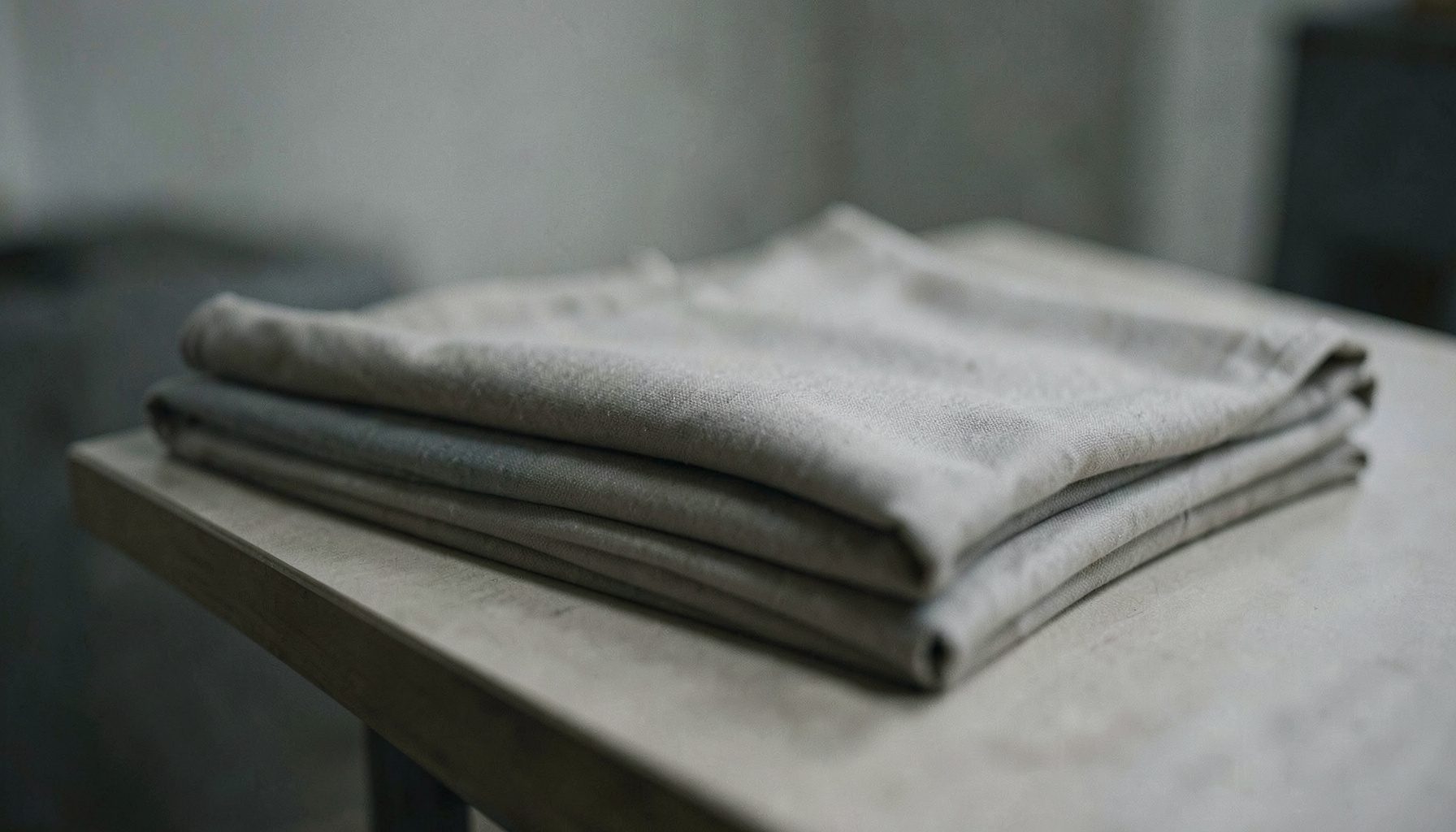 Close muted shot of folded neutral-toned drapery fabric samples stacked on a table, soft gray and beige palette, quiet minimal styling